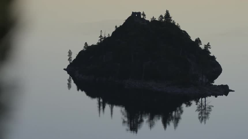 A large rock in the water has some trees on top