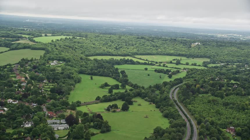 A huge rural area with several plots of grass and trees close to a village