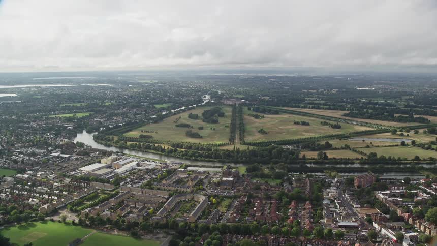 An aerial view of a suburban area in the middle of the day residential buildings are nestled amidst lush green vegetation a river acts as a natural barrier separating the suburbs from an open green field with a runway
