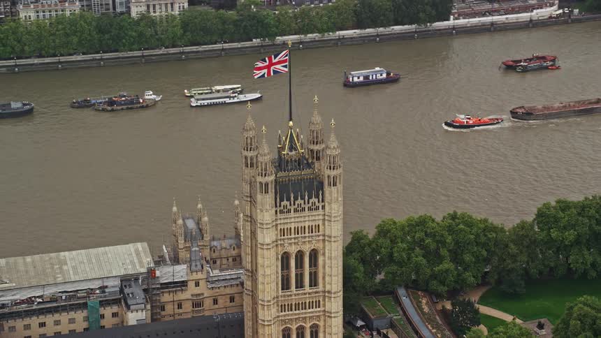 British flag tops tower of westminster palace near busy thames river
