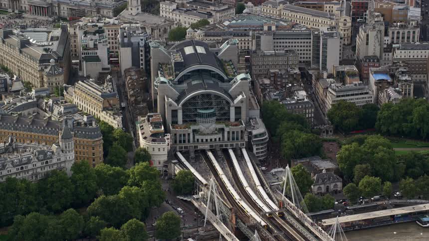 A bridge over a river with train tracks leading into a mega train station in a city with residential and high rise buildings