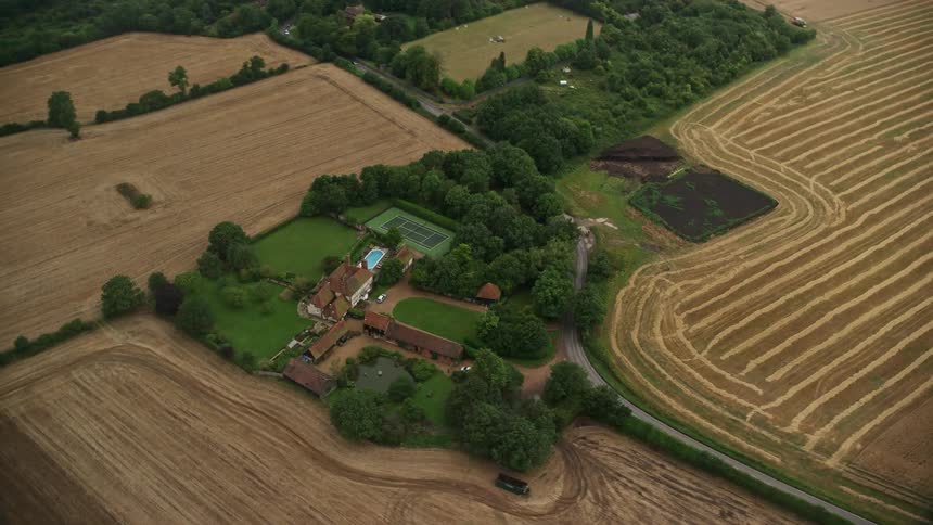 A house nestled in a rural area surrounded by abundant green vegetation with a cleared open field nearby