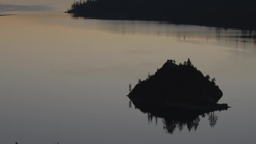 A large rock sits in this calm lake at sunset