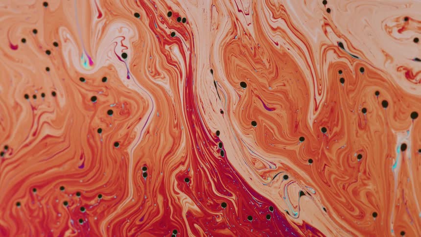 Black dots float in a pool of liquid orange stripes and they bend and twist as they mix