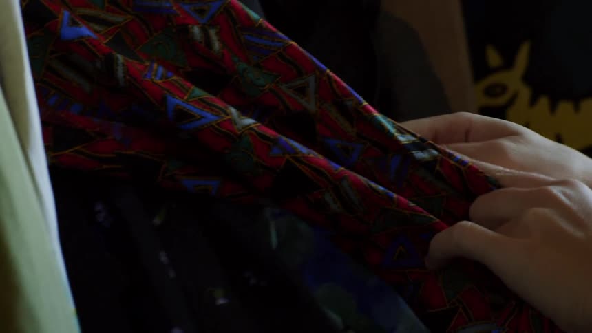 A person touches some clothing on a rack