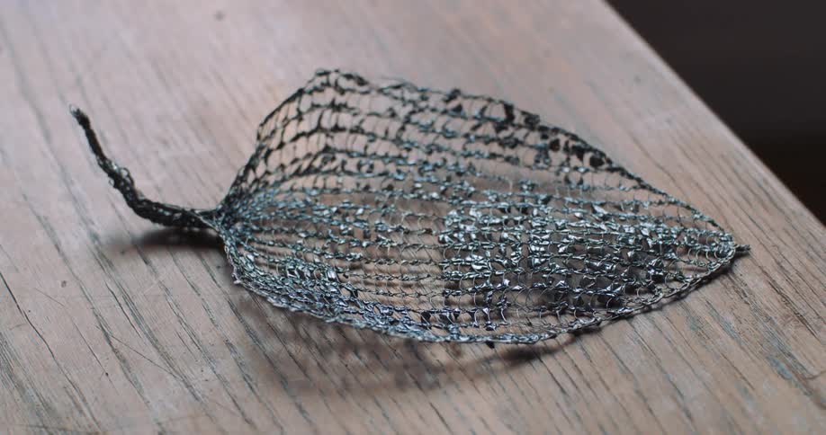 Wire sculpture of leaf lies on wooden table