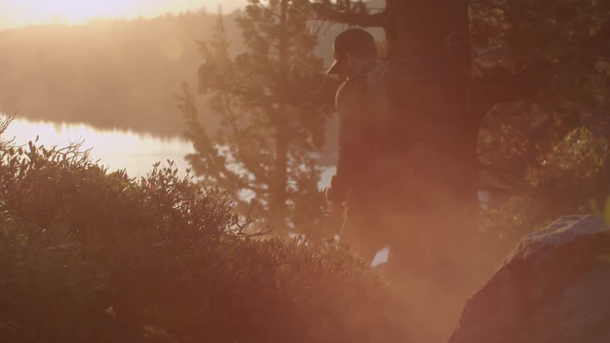 A man is hiking downhill towards a lake at sunset