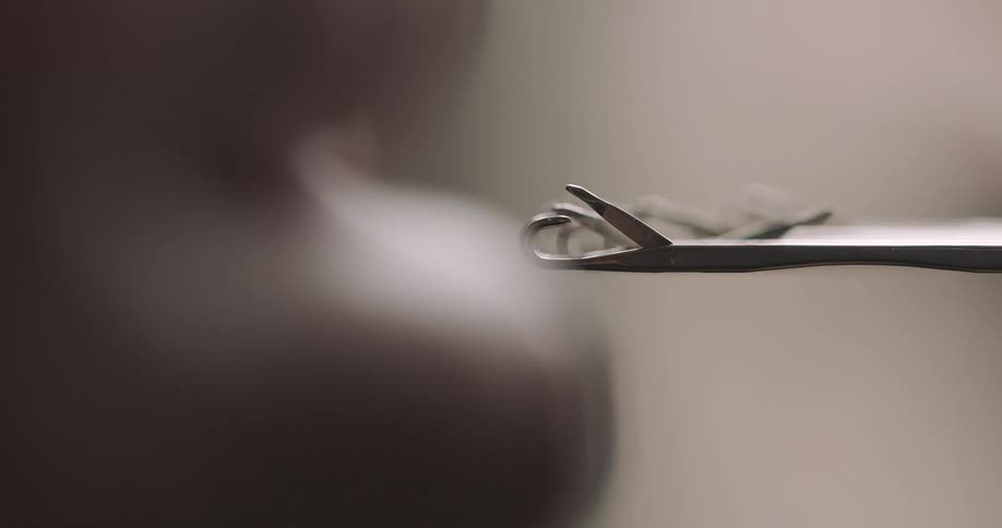 A closeup shot of a thumb and finger pulling a golden chain out of a metal clasp using a pointed metallic pencilshaped object