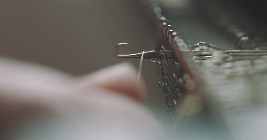 An adult is threading a metal clasp with a fine thread