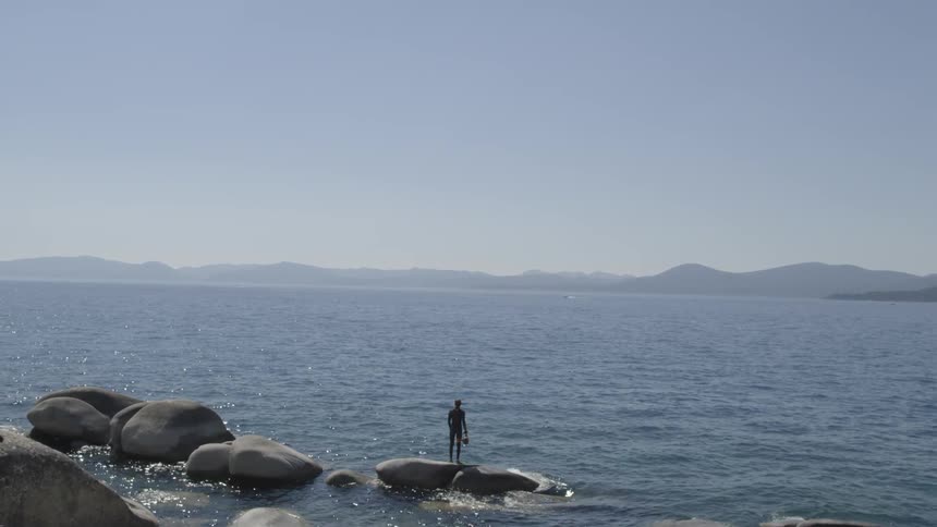 A man standing on top of a boulder as ocean waves wash against it