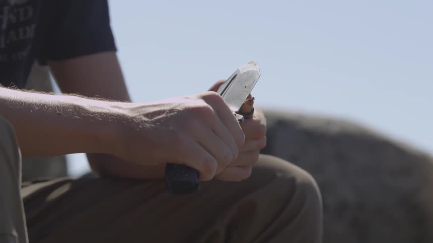 A man is sharpening a piece of wood with a knife