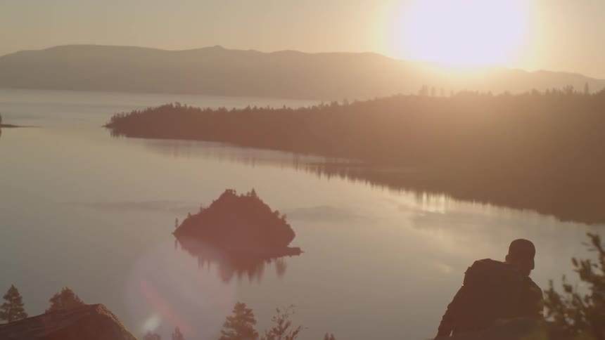 A man is hiking down a hill towards a lake