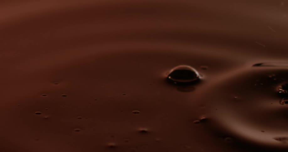 Liquid drops fall into chocolate brown fluid creating brown tinted splash