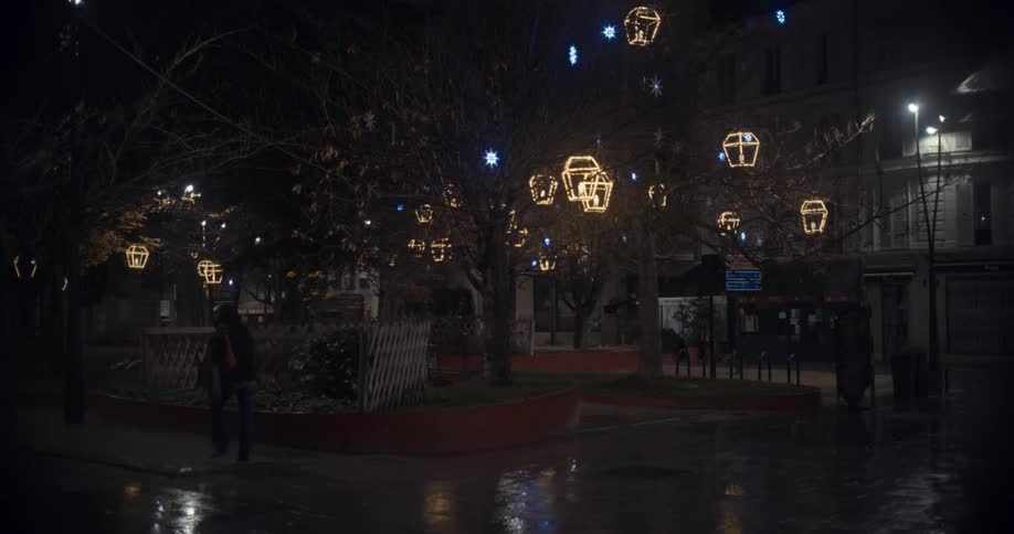 In the dark night there are christmass light and decoration in the middle of the street shining as people walk by