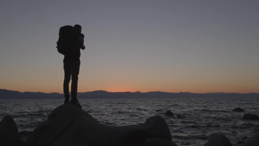 A man is standing on a rock near the water at dawn