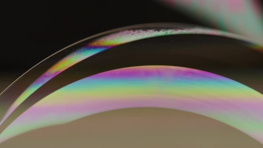 Iridescent ribbons curve over tan surface
