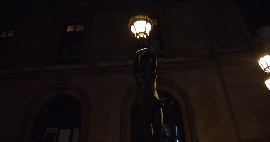 Lamp light held by a statue in front of a building in an urban environment during night time