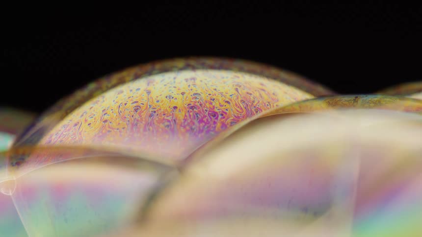 Multicolored mixture moves under filmy surface of soap bubbles