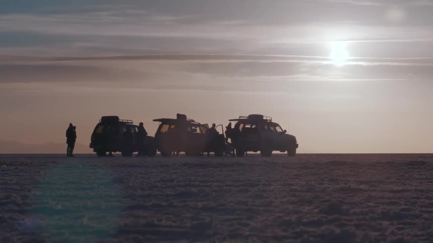 People are climbing out of three cars parked on icy plains at sunset