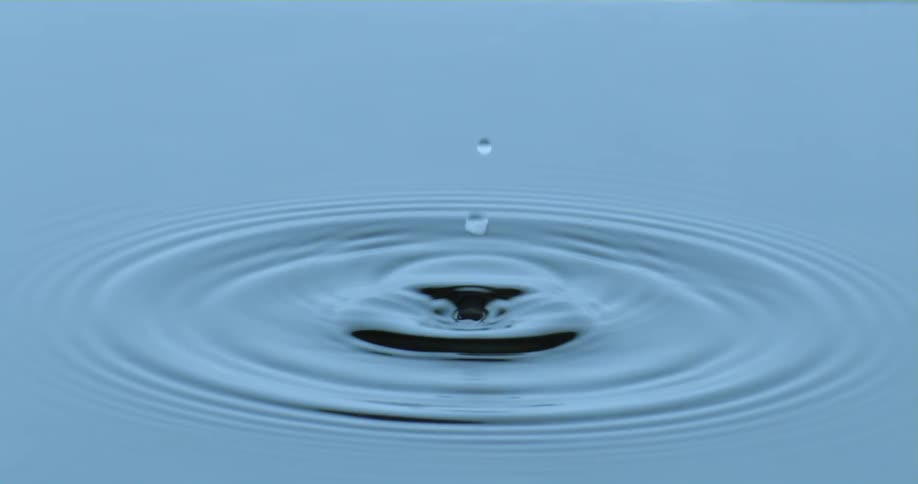 A droplet falls into the water as it splashes upward and ripples spread across the surface