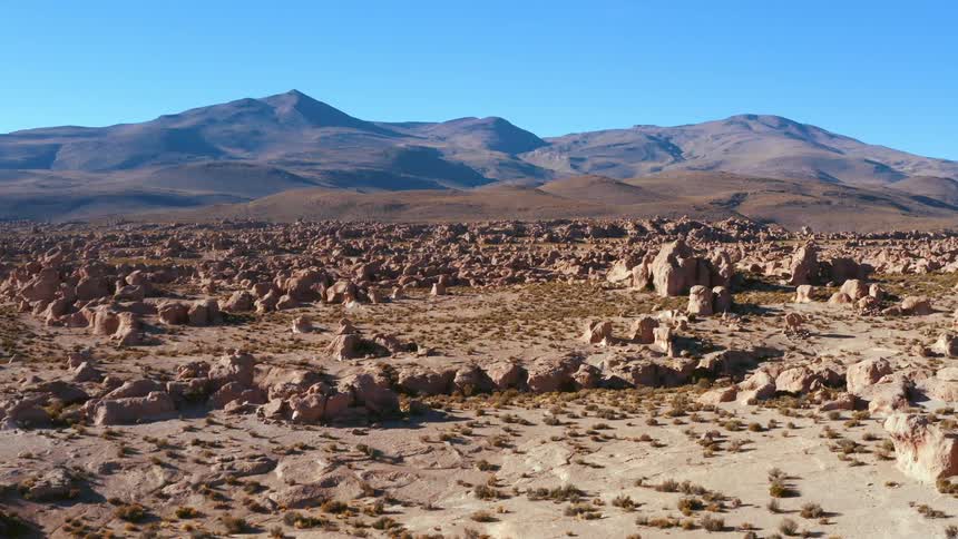 A midday landscape shot of a rocky badlands with distant peaks