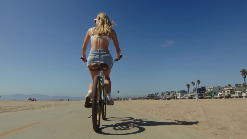 A woman on a bicycle is riding on a path through a sandy beach in the daytime