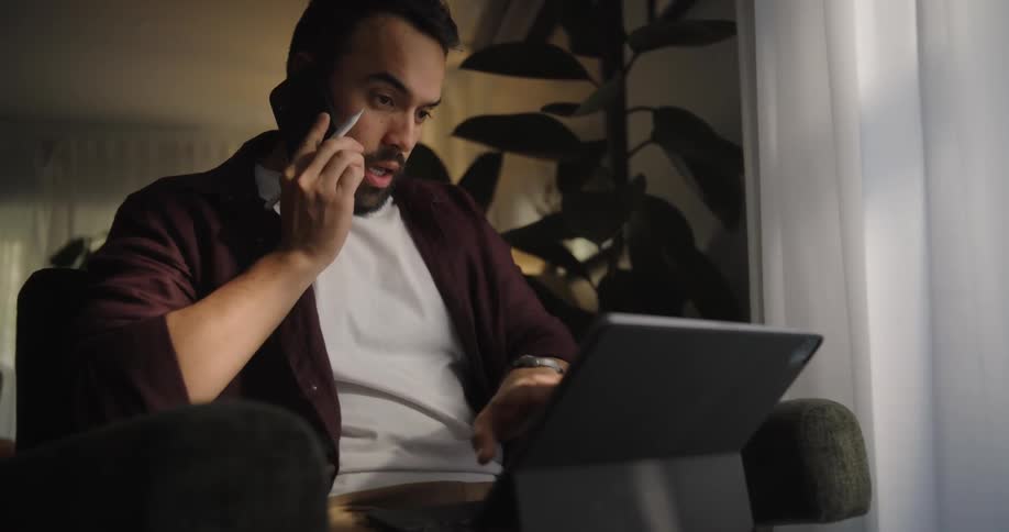 A man on a couch with a laptop talks on the phone and smiles