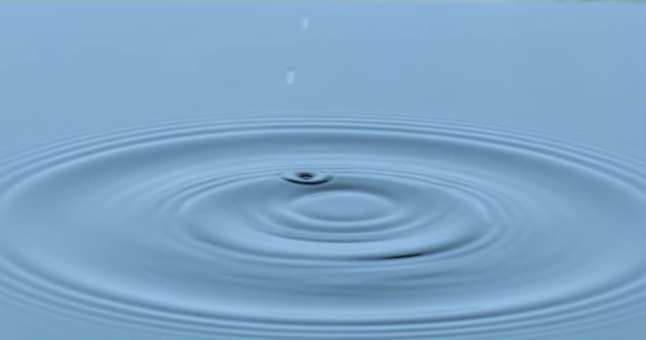 A droplet falls into the water as it splashes and ripples spread across the surface