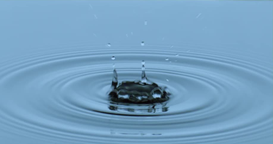 A droplet falls into the water as it splashes upward and ripples spread across the surface