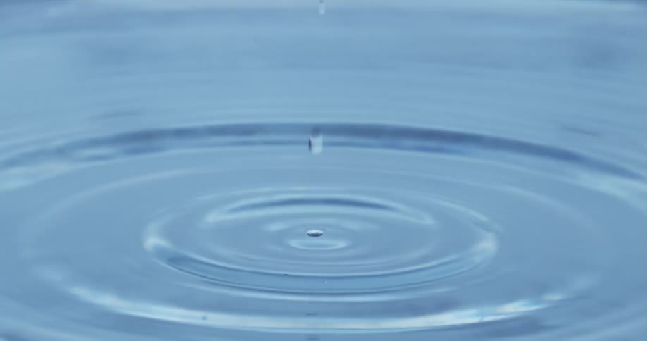 A drop of water lands on a body of water causing a splash