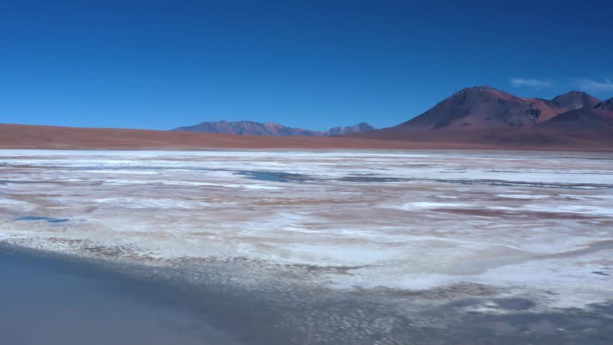 The ice is on the lake and the mountains are behind it with a rolling hill to the left of them