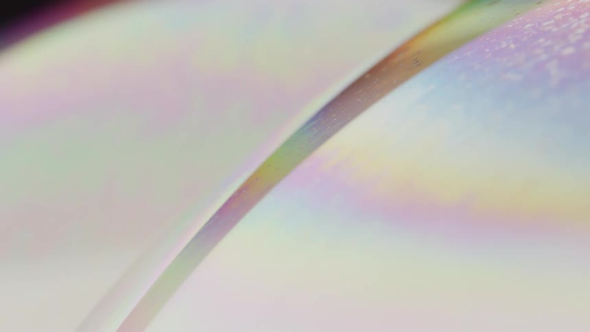 Heavy and light rainbow streaks cross over flowing pale liquid