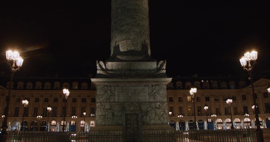 A pillar monument stands in a city square lit up at night with a visible inscription