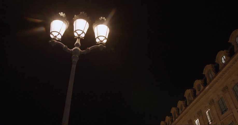 A streetlight shining in the middle of the night next to a residential building with light reflect out through the windows