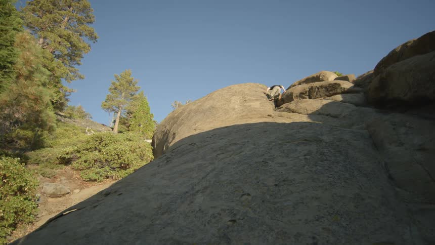 A man is climbing up the side of a cliff on a sunny day