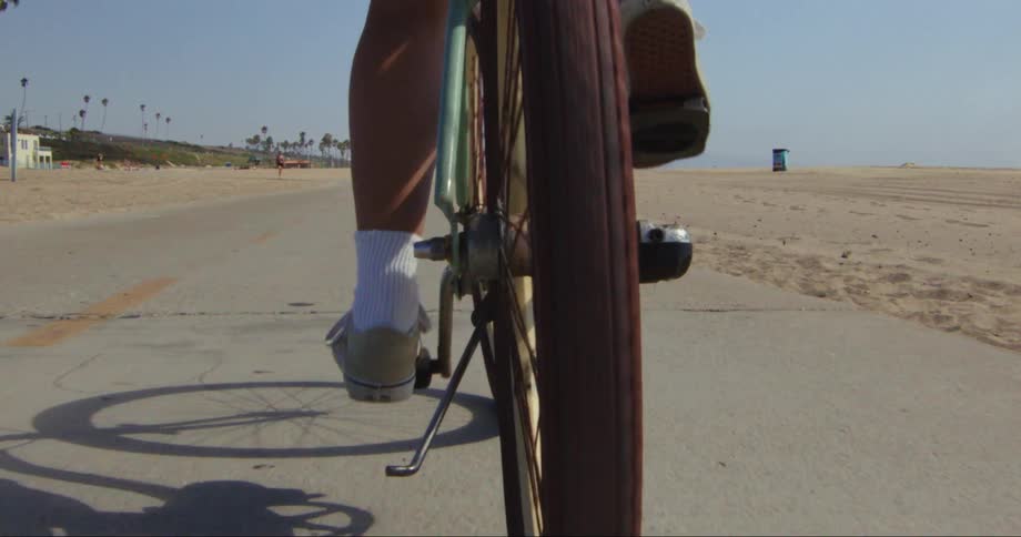 Person pedaling a bicycle on a path next to a beach