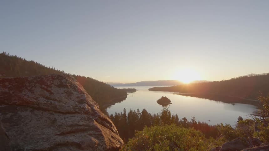 The sun is setting in the distance past this calm lake