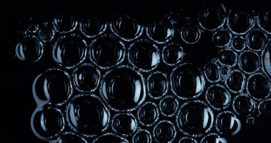 Liquid bubbles touching each other and bursting on a black background