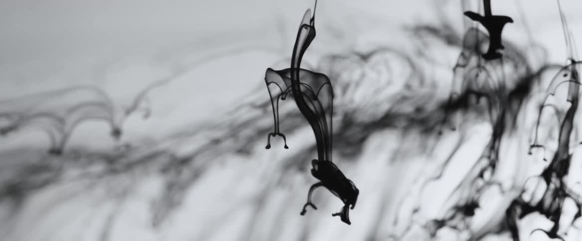 Black liquid streaks move downward in clear liquid in slow motion