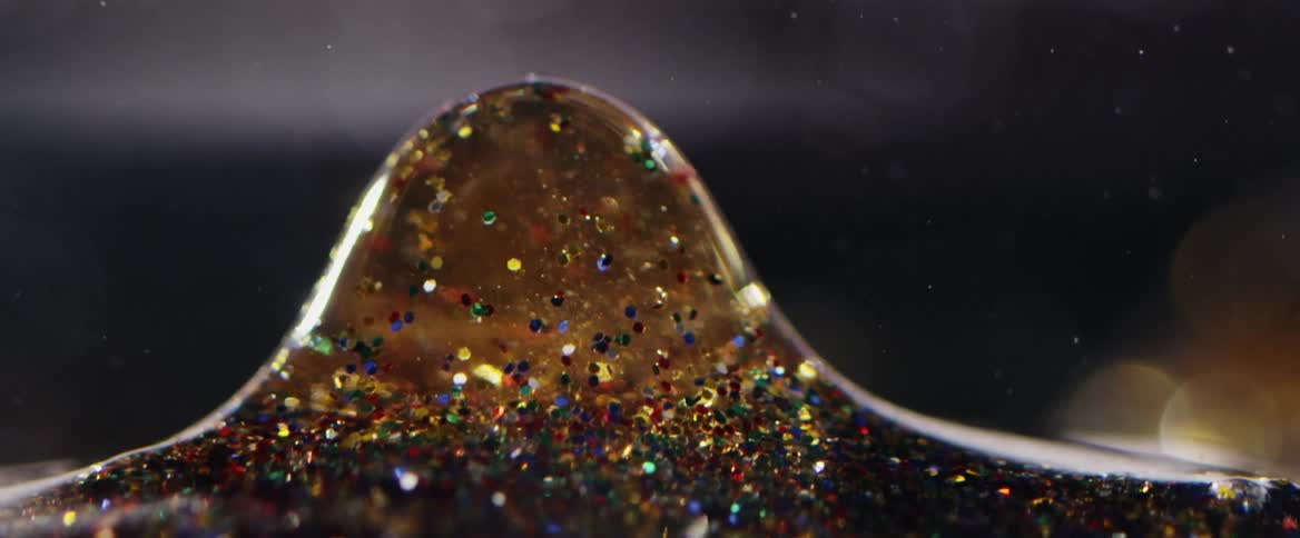 A golden liquid full of glitter is rising in the form of a bubble