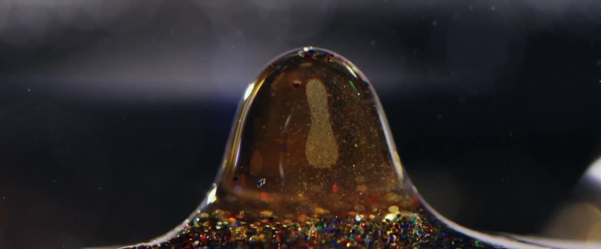 Thick syrup drips upside down from multicolored particles at base