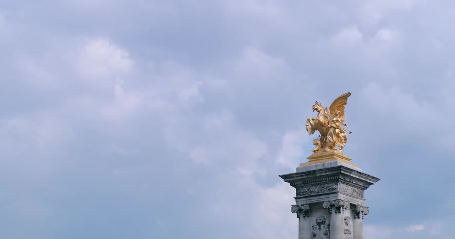 Golden winged sculpture tops decorated stone column under a cloudy sky