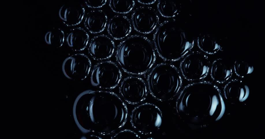 Bubbles touching each other and bursting against a black background