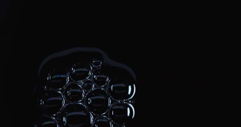 Light shines upon bubbles stuck together as they float across the darkness