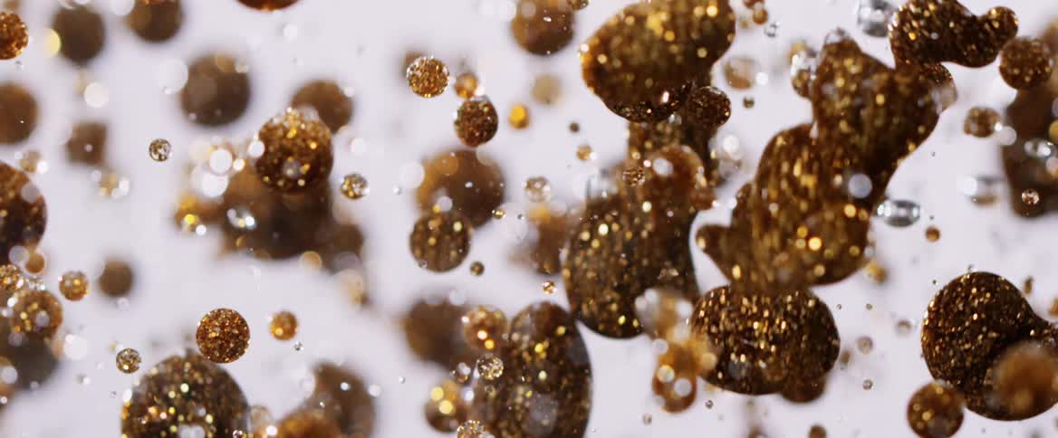 Gold glittery balls fall in a clear liquid in slow motion