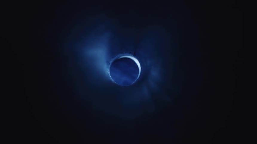 A large black hole in the center and a light passing through and illuminating with blue tones