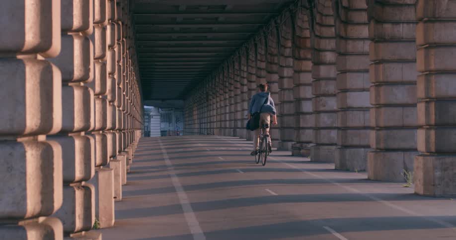 A man with a backpack is riding a bicycle on a street surrounded by pillars