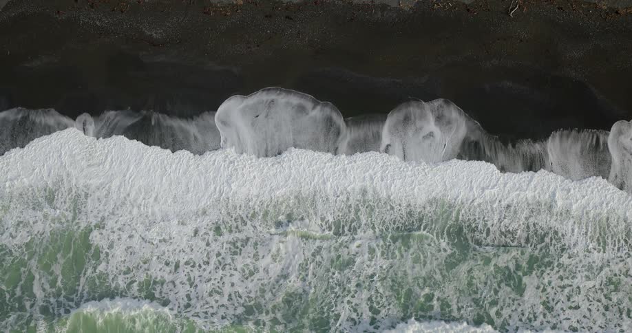 Aerial view of ocean waves on black sands