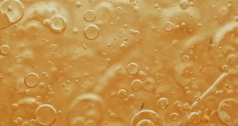 Yellow clear oily bubbles slowly floating around in liquid in a glass