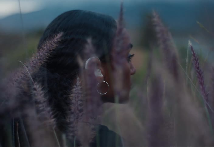 A woman sitting in a field of flowers wearing hearing aids